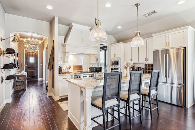 kitchen featuring hanging light fixtures, tasteful backsplash, an island with sink, custom range hood, and appliances with stainless steel finishes