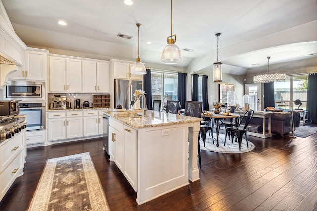 kitchen with light stone counters, a center island with sink, pendant lighting, and appliances with stainless steel finishes