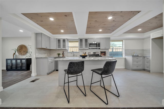 kitchen featuring light stone countertops, appliances with stainless steel finishes, a tray ceiling, a kitchen island, and wood ceiling