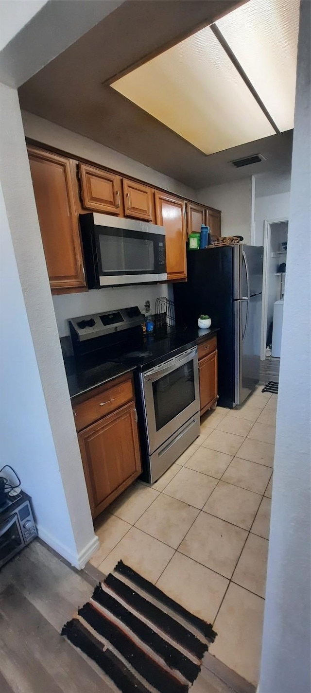 kitchen featuring appliances with stainless steel finishes, dark countertops, brown cabinets, and visible vents