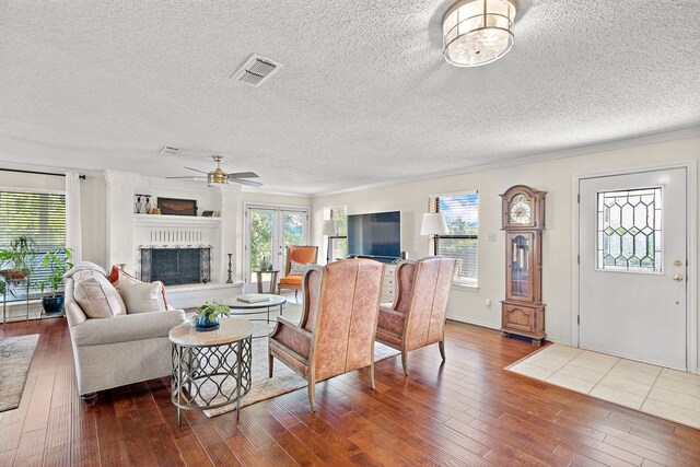 living room featuring hardwood / wood-style flooring, ceiling fan, crown molding, and a brick fireplace