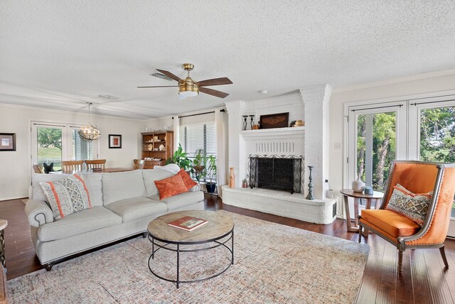 living room with a fireplace, ceiling fan with notable chandelier, wood-type flooring, and a textured ceiling