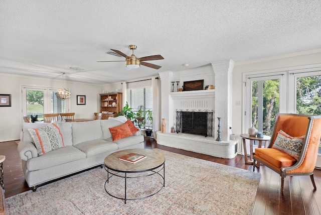 living room with crown molding, a fireplace, wood-type flooring, a textured ceiling, and ceiling fan with notable chandelier