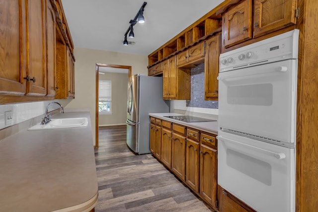 kitchen featuring black electric stovetop, backsplash, white double oven, sink, and stainless steel refrigerator