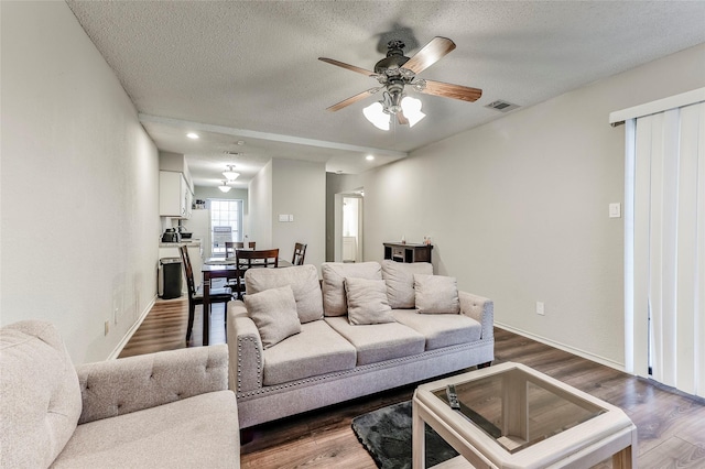 living room featuring ceiling fan, dark wood-type flooring, and a textured ceiling