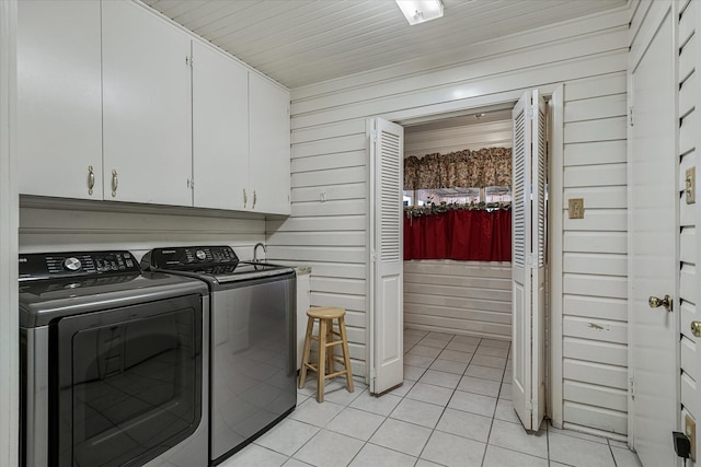 laundry area featuring light tile patterned floors, wood walls, independent washer and dryer, and cabinet space