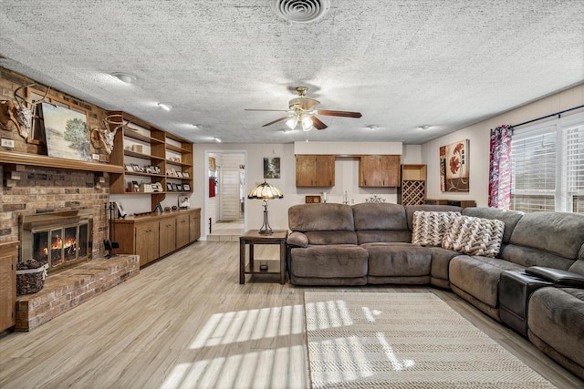 living room with light wood finished floors, visible vents, a ceiling fan, a brick fireplace, and a textured ceiling