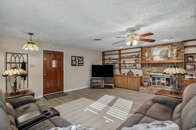 living area featuring a textured ceiling, a brick fireplace, light wood-style flooring, and built in features