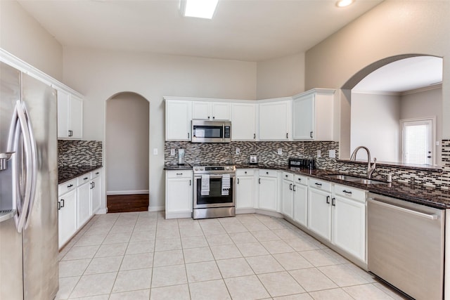 kitchen featuring appliances with stainless steel finishes, sink, light tile patterned floors, dark stone countertops, and white cabinets