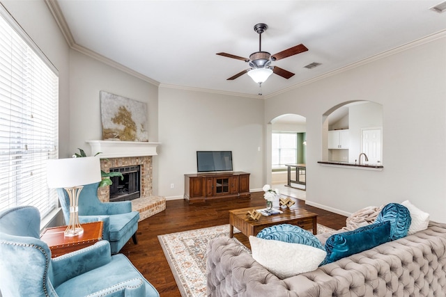 living room featuring crown molding, ceiling fan, dark hardwood / wood-style floors, and a brick fireplace