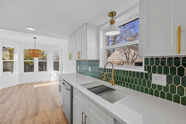 kitchen with pendant lighting, sink, stainless steel dishwasher, light wood-type flooring, and white cabinetry