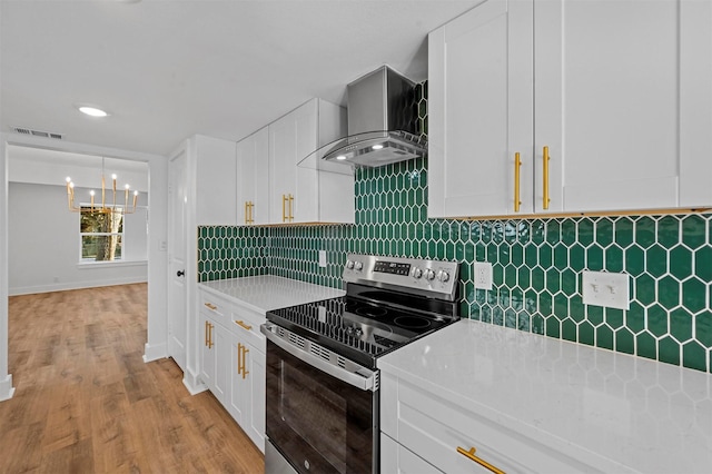 kitchen featuring light wood-type flooring, tasteful backsplash, wall chimney range hood, white cabinetry, and stainless steel range with electric cooktop