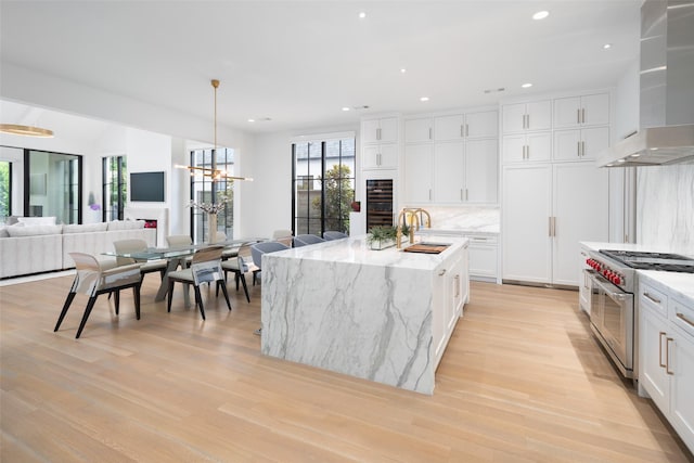 kitchen featuring white cabinetry, sink, wall chimney exhaust hood, double oven range, and a kitchen island with sink