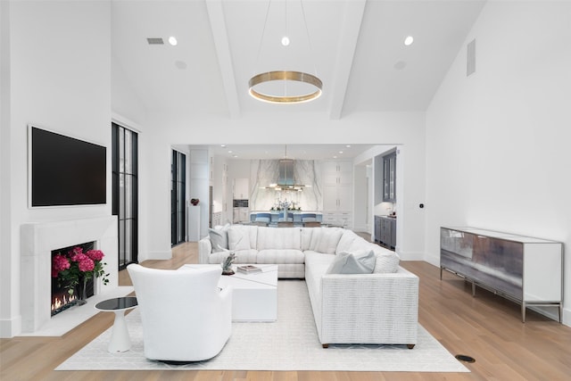 living room featuring beam ceiling, a towering ceiling, and light hardwood / wood-style floors