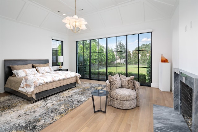 bedroom featuring hardwood / wood-style flooring, a tiled fireplace, a notable chandelier, and coffered ceiling