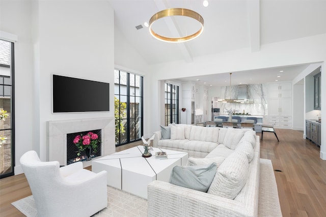 living room with beamed ceiling, light hardwood / wood-style floors, a fireplace, and high vaulted ceiling