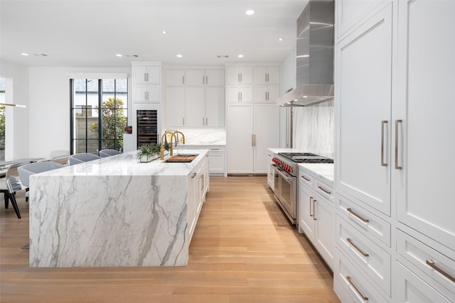 kitchen with range with two ovens, a kitchen island with sink, wall chimney exhaust hood, and sink