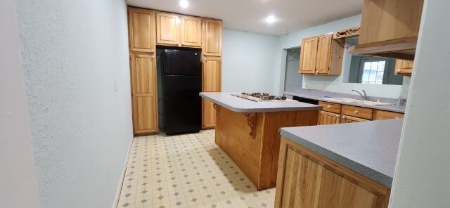 kitchen featuring stainless steel gas stovetop, a center island, a breakfast bar, black refrigerator, and sink