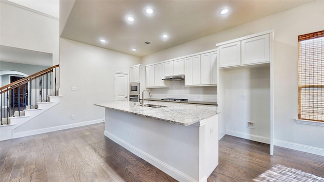 kitchen with light stone countertops, appliances with stainless steel finishes, sink, white cabinetry, and an island with sink