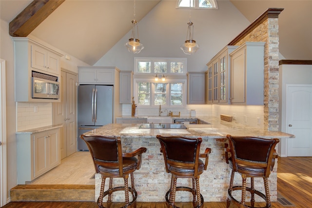 kitchen featuring a kitchen bar, tasteful backsplash, built in microwave, high vaulted ceiling, and stainless steel refrigerator