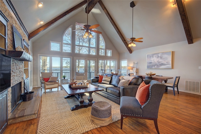 living room featuring high vaulted ceiling, hardwood / wood-style flooring, ceiling fan, beamed ceiling, and a large fireplace