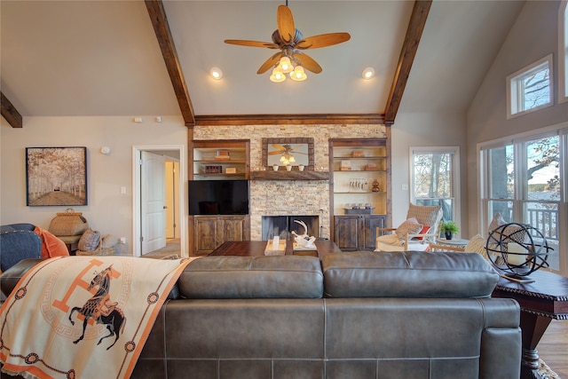 living room with a stone fireplace, ceiling fan, built in shelves, and lofted ceiling with beams