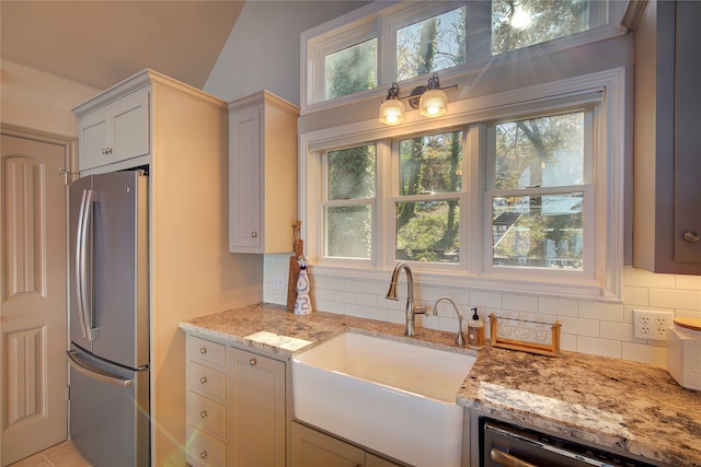 kitchen with lofted ceiling, sink, decorative backsplash, light stone countertops, and appliances with stainless steel finishes