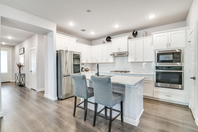 kitchen featuring stainless steel appliances, an island with sink, a breakfast bar area, and white cabinets