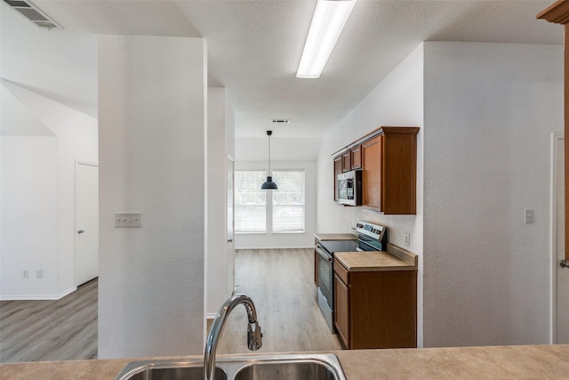 kitchen featuring appliances with stainless steel finishes, light hardwood / wood-style flooring, hanging light fixtures, and sink