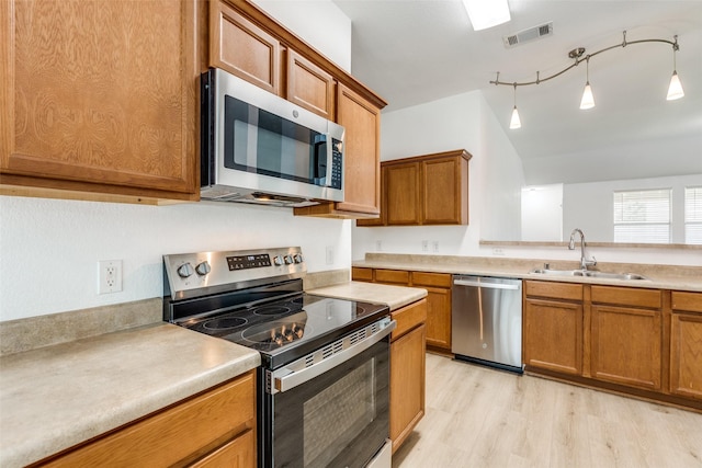 kitchen with decorative light fixtures, vaulted ceiling, light hardwood / wood-style floors, sink, and stainless steel appliances