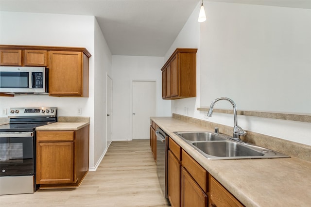 kitchen featuring decorative light fixtures, sink, stainless steel appliances, and light hardwood / wood-style flooring