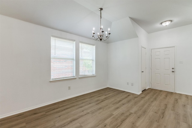 empty room with lofted ceiling, light wood-type flooring, and an inviting chandelier