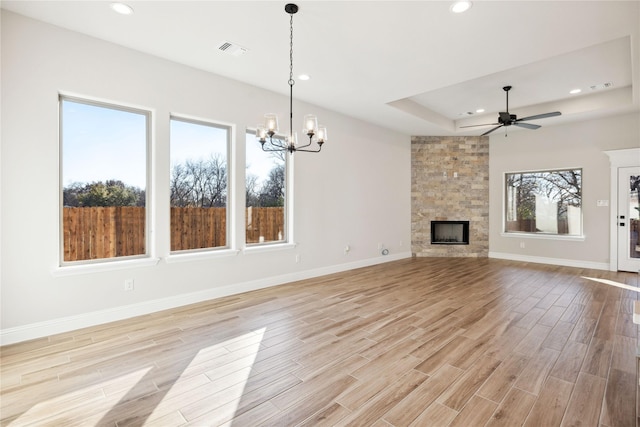 unfurnished living room with ceiling fan with notable chandelier, a raised ceiling, and a fireplace