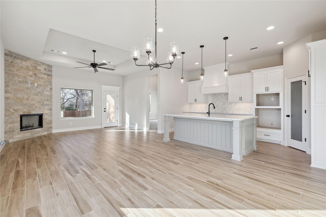 kitchen featuring ceiling fan with notable chandelier, a tray ceiling, decorative light fixtures, white cabinetry, and an island with sink