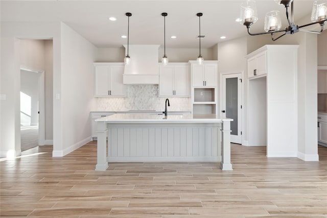 kitchen with decorative backsplash, a kitchen island with sink, decorative light fixtures, a chandelier, and white cabinetry