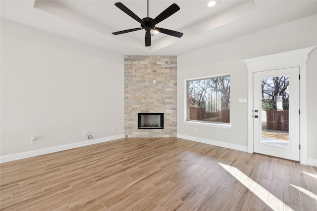 unfurnished living room featuring a raised ceiling, ceiling fan, and a fireplace