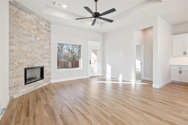 unfurnished living room with a tile fireplace, light hardwood / wood-style flooring, a raised ceiling, and ceiling fan