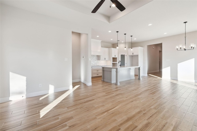 kitchen with white cabinetry, backsplash, pendant lighting, a spacious island, and ceiling fan with notable chandelier