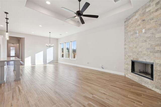 unfurnished living room with a tile fireplace, ceiling fan with notable chandelier, and a tray ceiling