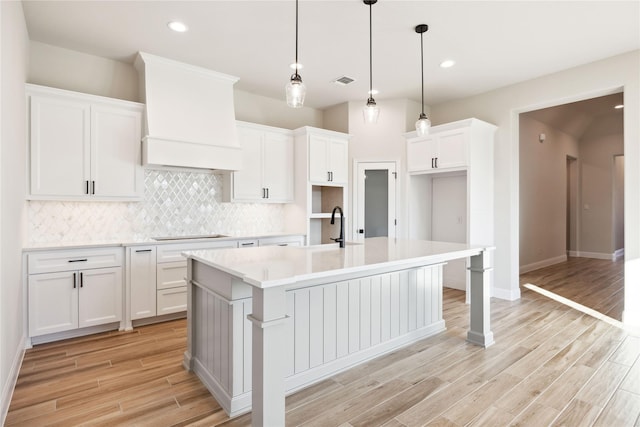 kitchen with backsplash, a center island with sink, black electric cooktop, decorative light fixtures, and white cabinetry