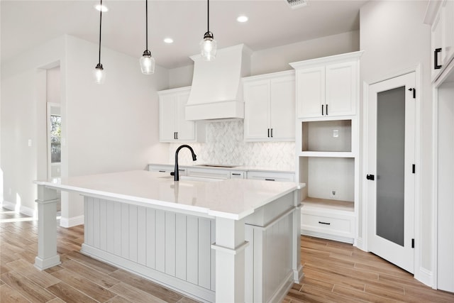 kitchen with white cabinets, decorative light fixtures, a kitchen island with sink, and custom exhaust hood