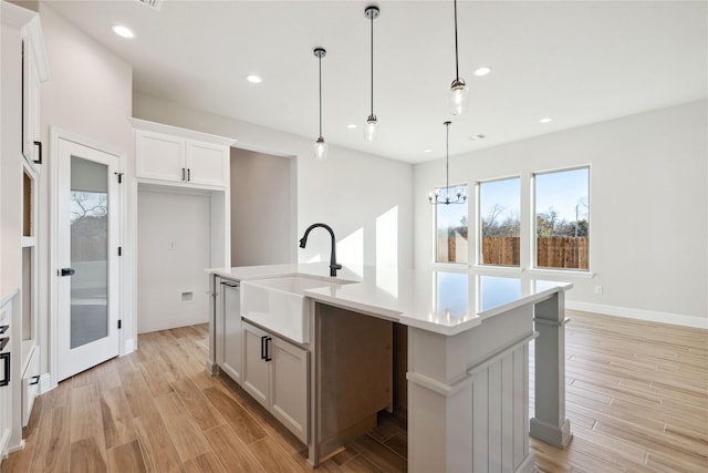 kitchen with light wood-type flooring, sink, decorative light fixtures, a center island with sink, and white cabinets