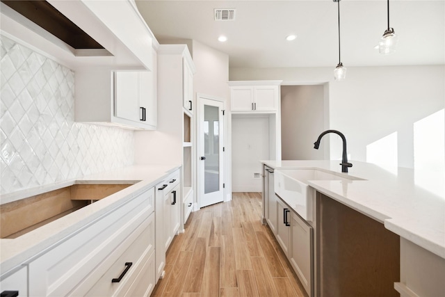 kitchen featuring white cabinets, sink, light hardwood / wood-style flooring, tasteful backsplash, and decorative light fixtures