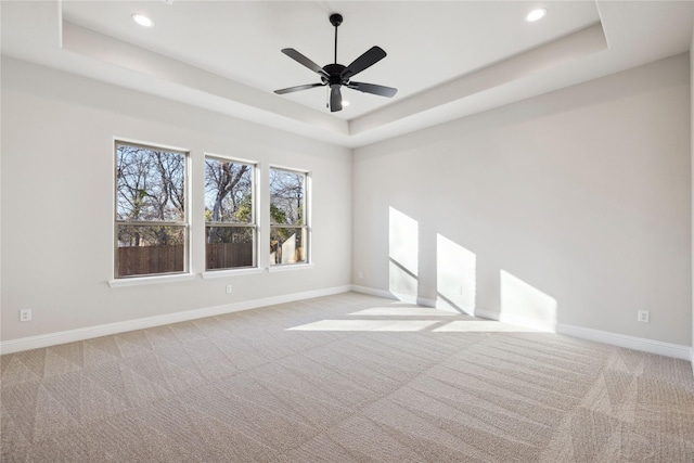 empty room featuring ceiling fan, a raised ceiling, and light colored carpet