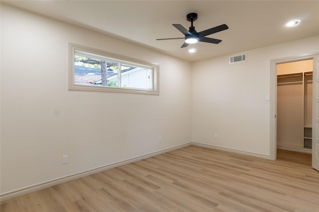 unfurnished bedroom featuring a spacious closet, a closet, ceiling fan, and light wood-type flooring