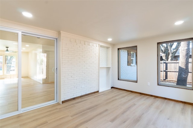 unfurnished room featuring brick wall and light hardwood / wood-style flooring