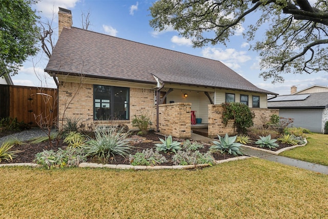 view of front of property with a front lawn, roof with shingles, a chimney, and brick siding