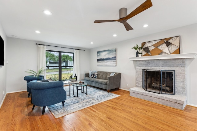 living room featuring a brick fireplace, hardwood / wood-style floors, and ceiling fan