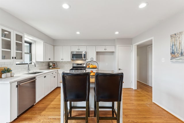 kitchen with appliances with stainless steel finishes, light wood-type flooring, a sink, and tasteful backsplash