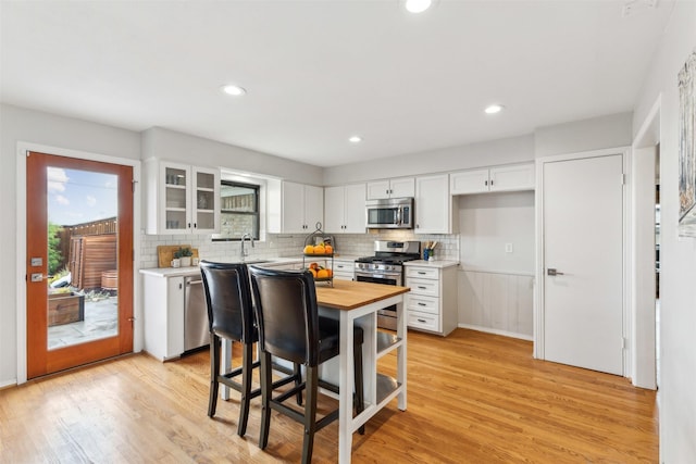 kitchen with tasteful backsplash, appliances with stainless steel finishes, white cabinetry, butcher block countertops, and light wood-type flooring